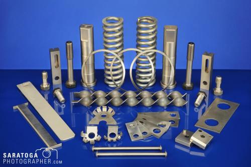 Fanned out display of various manufactured metal parts including springs shims lifters and bolts on blue background