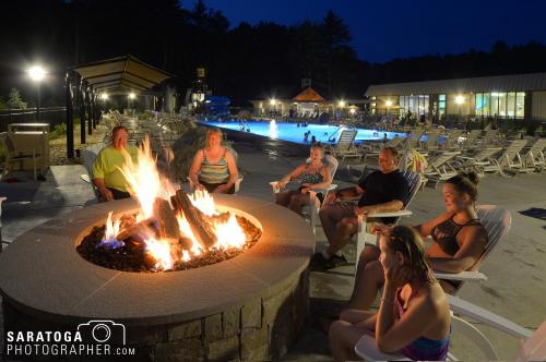 Twilight photo of group of young adults around fire pit on the patio with lounge chairs and swimming pool in background